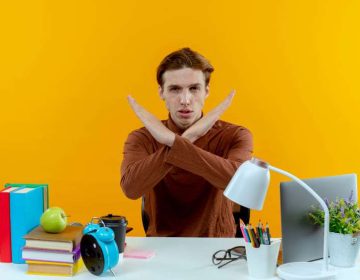 joven-sentado-escritorio-mostrando-gesto-no